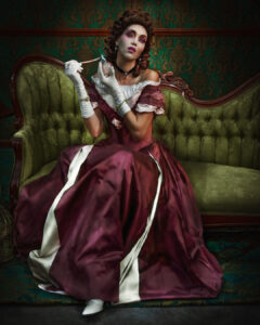 Model in flowing burgundy dress, on green couch, dramatic 19th century look, painterly drama