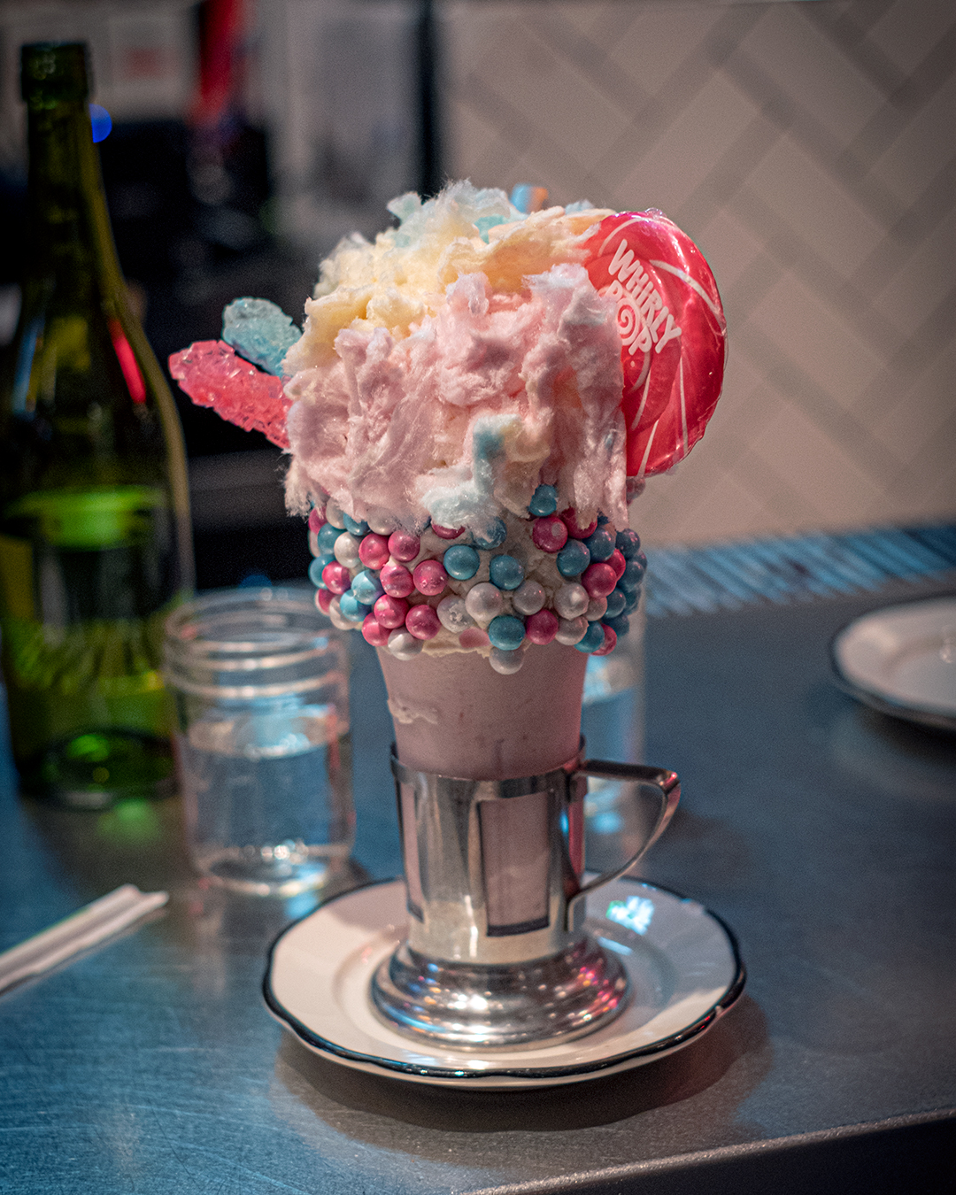 Milkshake with pink cotton candy, lolipop and blue and pink gumballs and blue and pink rock candy.